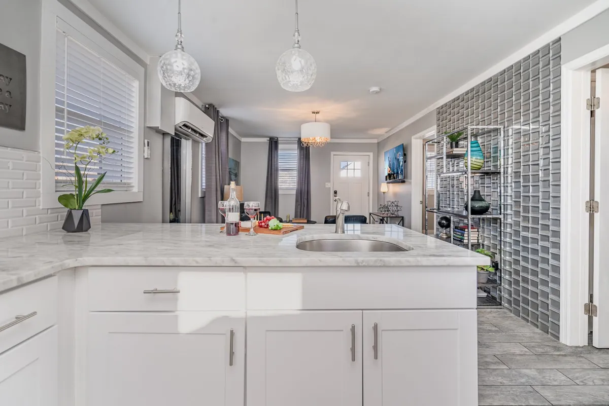 An inviting open-plan kitchen and dining area with a kitchen island, hanging pendant lights, a decorative shelving unit, and a visible dining table. The space is set up for cooking, entertaining, and shared meals, with a stylish and modern touch.