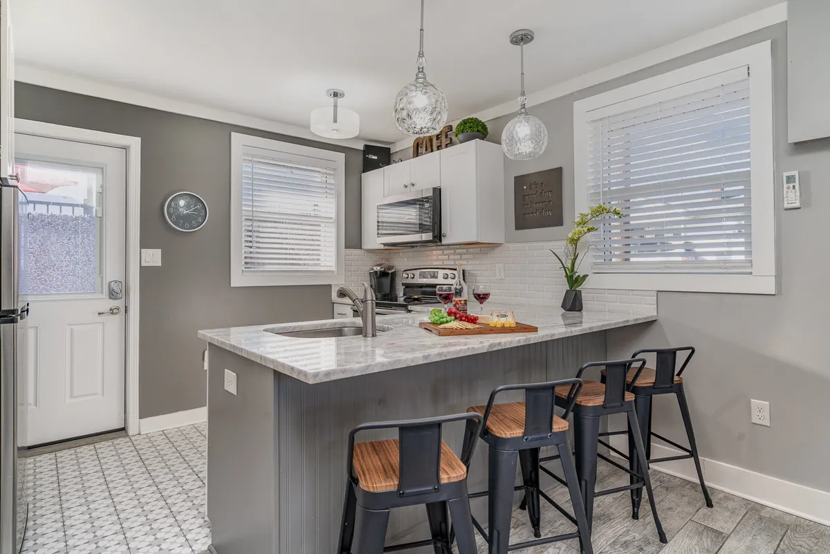 A bright, modern kitchen with a large kitchen island, bar stools for four, a countertop arrangement of food and drinks, and stylish pendant lighting. The image captures an inviting space perfect for casual dining, meal prep, and social gatherings.