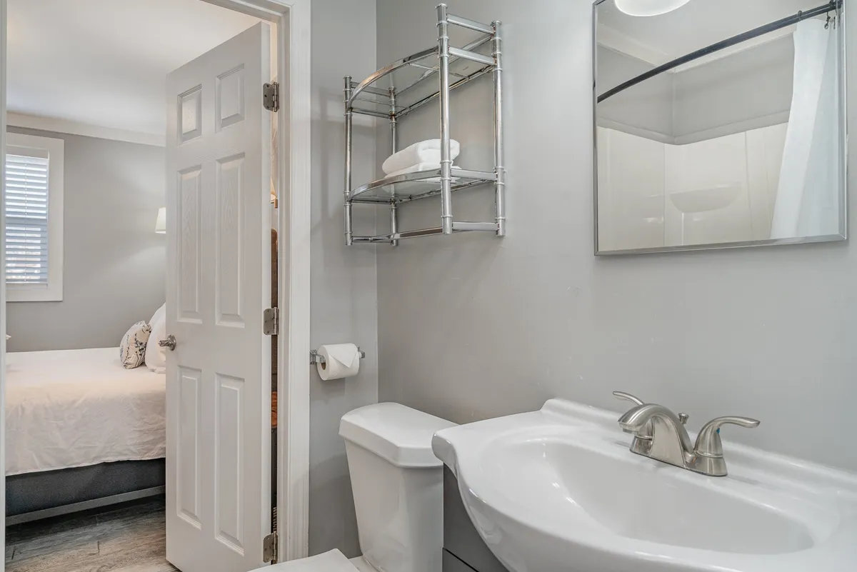 A bright and functional Jack-n-Jill style bathroom with a modern sink, mirror, toilet, and towel rack. Fresh towels are neatly arranged, and natural light streams in, creating an inviting space for morning routines.
